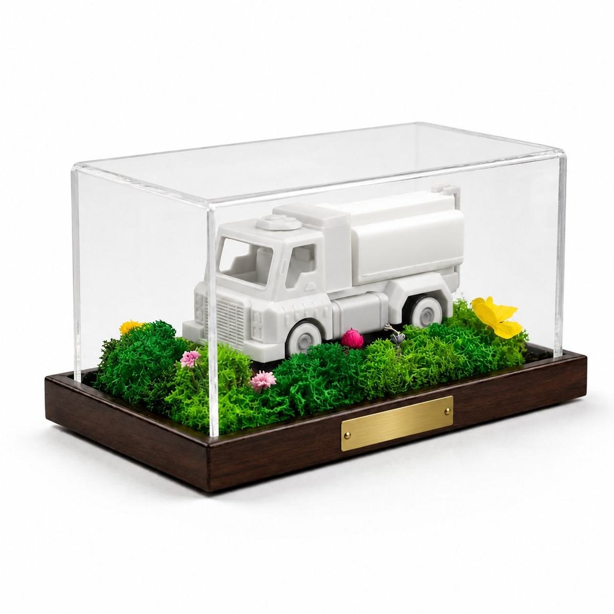 A plain white model truck in a moss landscape under a clear case, with a blank brass plate